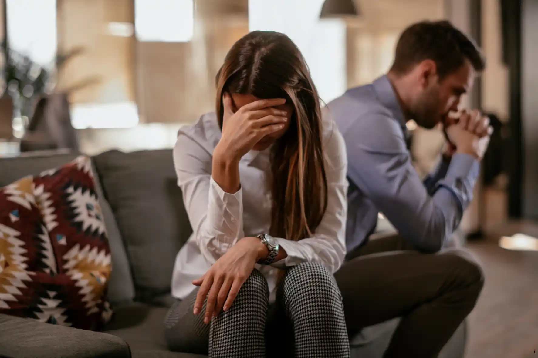Ein Paar sitzt auf der Couch, voneinander abgewandt. Sie sind unglücklich in der Beziehung